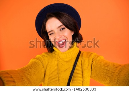 Self photo of winking cute nice friendly fooling girl wearing cap showing her flirty nature while isolated with orange background