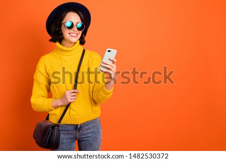 Copyspace photo of cheerful nice beautiful modern luxurious girlfriend browsing through her phone in search of sales and discounts while isolated with orange background