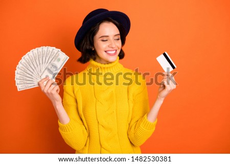Photo of pensive thinking girlfriend interested what way of payment is better while isolated with orange background while wearing cap