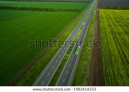 green truck driving on asphalt road along the green fields. seen from the air. Aerial view landscape. drone photography.  cargo delivery