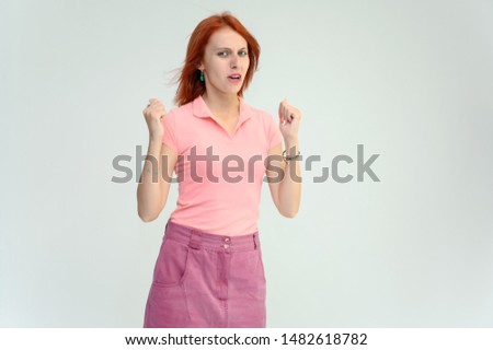 Photo Portrait of a cute woman girl with bright red hair in a peach t-shirt and pink skirt on a white background in studio. He talks, shows his hands in front of the camera with emotions.