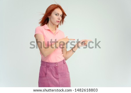 Photo Portrait of a cute woman girl with bright red hair in a peach t-shirt and pink skirt on a white background in studio. He talks, shows his hands in front of the camera with emotions.