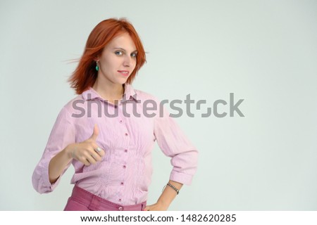 Photo Portrait of a cute girl woman with bright red hair manager in a pink shirt on a white background in studio. He talks, shows his hands in front of the camera with emotions.