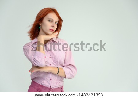 Photo Portrait of a cute girl woman with bright red hair manager in a pink shirt on a white background in studio. He talks, shows his hands in front of the camera with emotions.