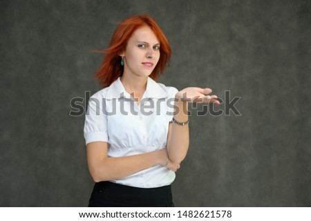 Photo Portrait of a cute girl woman with bright red hair manager in a white shirt on a gray background in the studio. He talks, shows his hands in front of the camera with emotions.