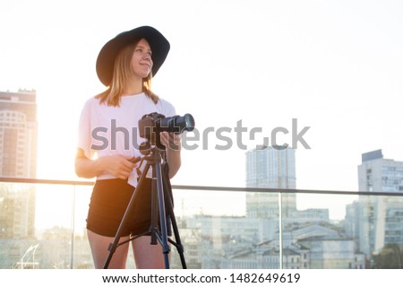 young girl photographer with a camera and a tripod on a background of the city, she photographs at sunset, a woman shoots a video