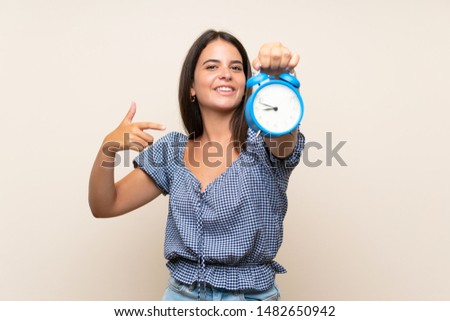 Young girl over isolated background holding vintage alarm clock