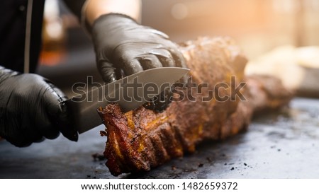 Grill restaurant kitchen. Chef in black cooking gloves using knife to cut smoked pork ribs. Royalty-Free Stock Photo #1482659372