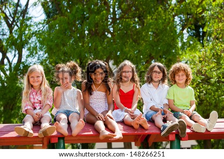 Portrait of happy children sitting together wooden structure in park.