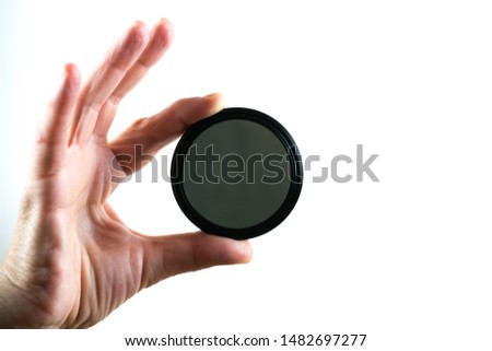 Hand holding neutral density filter for photographic lens. On white background.