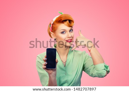 Call me. Closeup redhead young woman pretty smiling pinup girl green button shirt showing phone screen giving call me sign hands gesture looking at you camera, retro vintage 50's hairstyle on pink