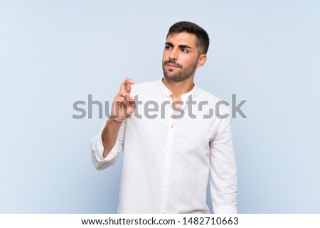 Handsome man with beard over isolated blue background with fingers crossing and wishing the best