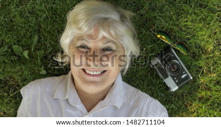 Senior female tourist lies on grass and smile. Camera and sunglasses. Leisure, vacations, tourism concept