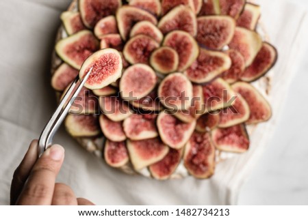 A girls hand holding a pair of culinary pliers preparing fig fruit garnish on a meringue cake. 