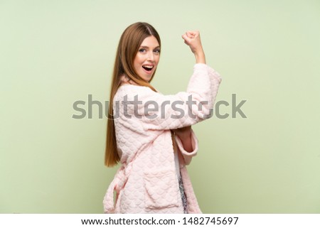 Young woman in dressing gown over green wall making strong gesture
