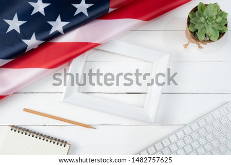 Top view of keyboard, book, pencil, white photo frame and American flag on white wooden background. Happy Labor Day.