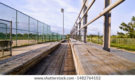 close up shot of the wooden benches in the grandstand of an empty softball field, showing straight lines that seem to meet at some point in the distance