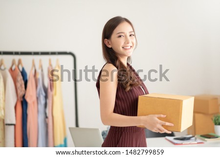 Portrait of Successful Asian woman fashion designer standing and holding cardboard box. Startup of Business owner. Beautiful Girl smiling and Looking at camera. SME. Royalty-Free Stock Photo #1482799859