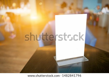 Mock up Label the blank menu frame in Bar restaurant ,Stand for booklets with white sheets paper acrylic tent card on wooden table cafeteria blurred background can inserting the text of the customer. 