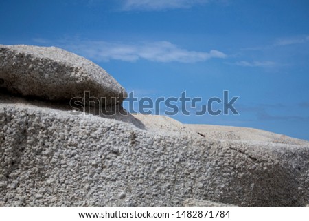 Sunlit large boulders on cloudy blue sky background. Perfect image for creation of the different types of collages, illustrations and digital media. Grey and blue colors combination. 