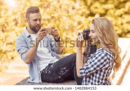 Man and woman taking photos with a camera and a smartphone in autumn park.