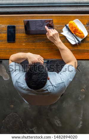 Vertical photo of Asian freelancer using tablet at cafeteria
