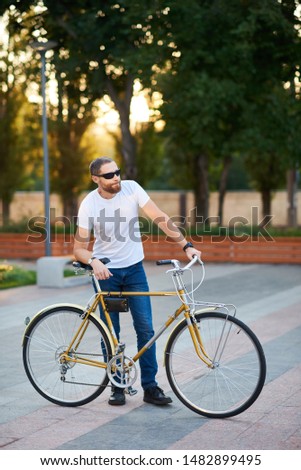 The red bearded man in casual clothes is cycling on the road in the morning city. Healthy lifestyle concept