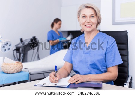 Mature female doctor cosmetologist working with documents in modern cosmetic office