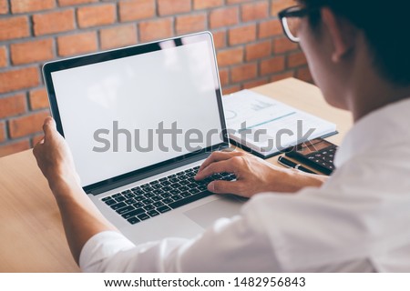 Image of Young man working in front of the laptop looking at screen with a clean white screen and blank space for text and hand typing information on keyboard in modern workspace. Royalty-Free Stock Photo #1482956843