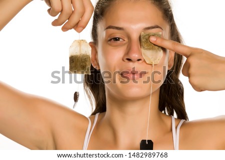 Young smiling woman posing with tea bag on her eye on white background Royalty-Free Stock Photo #1482989768