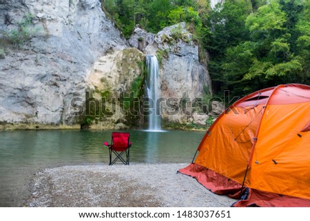 They are camping in Ilica waterfall with orange colored tent and red chairs. Contrasting colors created a beautiful image. Kastamonu, Turkey Royalty-Free Stock Photo #1483037651