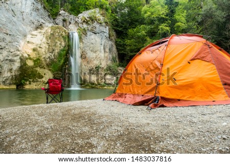 They are camping in Ilica waterfall with orange colored tent and red chairs. Contrasting colors created a beautiful image. Kastamonu, Turkey Royalty-Free Stock Photo #1483037816