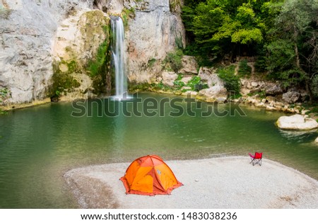 They are camping in Ilica waterfall with orange colored tent and red chairs. Contrasting colors created a beautiful image. Kastamonu, Turkey Royalty-Free Stock Photo #1483038236