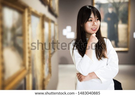 Portrait of attentive chinese young woman near picture collection in the museum