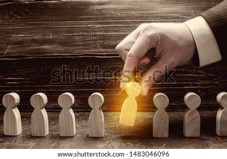 A businessman pulls a glowing golden man figure out of a gray crowd. The concept of search workers for hiring, promotion. Business management. Talented and capable employee, selection of candidates. Royalty-Free Stock Photo #1483046096