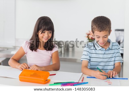 Smiling siblings drawing with their markers in kitchen at home