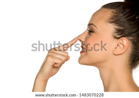 profile of young happy woman touches her nose with her finger on a white background Royalty-Free Stock Photo #1483070228