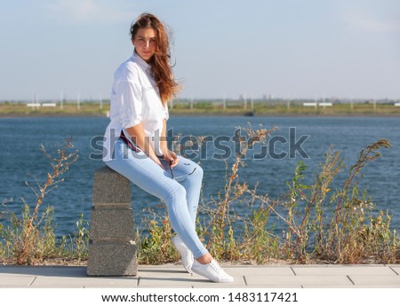 Picture of smiling pretty girl sitting on fence in park. Portrait.