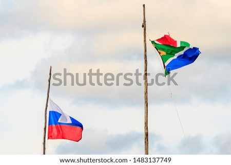 Flag of Russia and South Africa on wooden flagpoles on background of blue sky with white clouds. South Africa and Russia flag waving in wind against cloudy together. Diplomacy concept, international