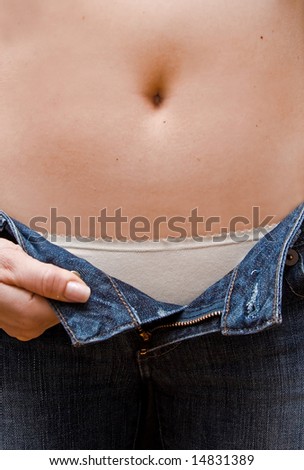 Young woman opening her blue jeans showing a rim of her white underwear and bare belly up to her bellybutton