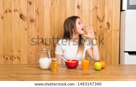 Young blonde woman having breakfast shouting with mouth wide open