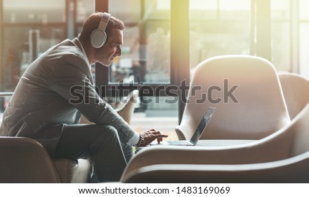 Portrait of focused middle-aged businessman in headphones listening to audio business course at work. E-learning and online professional education concept. Horizontal shot. Side view