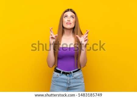 Young woman over isolated yellow background with fingers crossing and wishing the best