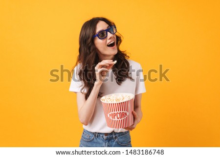 Photo of happy smiling young woman posing isolated over yellow wall background eat popcorn watch film looking aside.