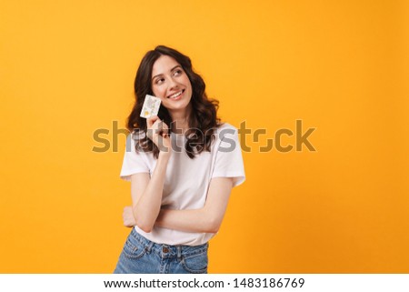 Photo of happy smiling dreaming young woman posing isolated over yellow wall background holding debit card.