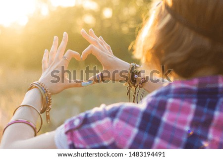 A girl showing hands the sign of the heart in the sun, enjoying life and showing love to the outside world.