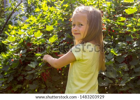 Pretty little girl stands by the way with ripe red currant berries with a smile on her face