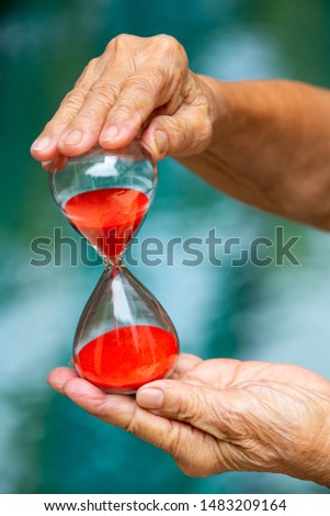 Senior woman's hands holding red hourglass in blue swimming pool background, Close up & Macro shot, Selective focus, Time concept
