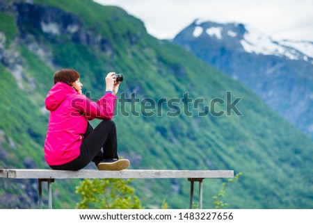 Tourism adventure and travel. Female tourist hiker sitting on bench in stone mountains taking photo with camera, looking at scenic view, Norway Scandinavia.