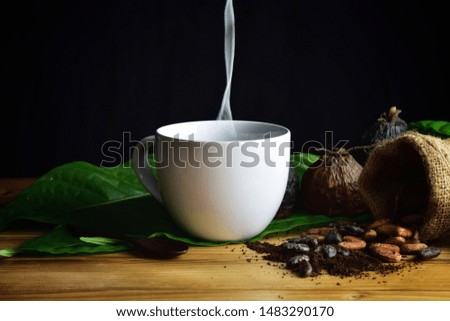 black cocoa hot drink on white cup with cocoa pods and  green leaf cocoa Seed and cocoa nibs on wooden table.  ,Sugar free beverages concept 
